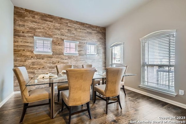 dining room featuring dark wood-style floors, an accent wall, and baseboards