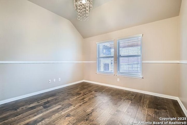 unfurnished room with lofted ceiling, dark wood-style flooring, a notable chandelier, and baseboards