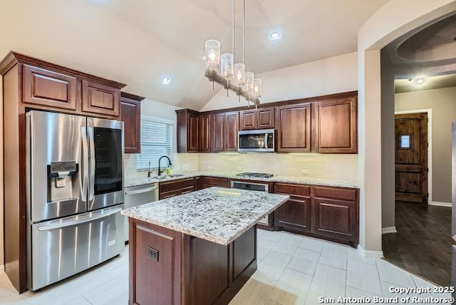 kitchen with stainless steel appliances, hanging light fixtures, backsplash, a kitchen island, and light stone countertops