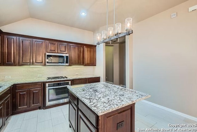 kitchen featuring pendant lighting, stainless steel appliances, decorative backsplash, a kitchen island, and light stone countertops