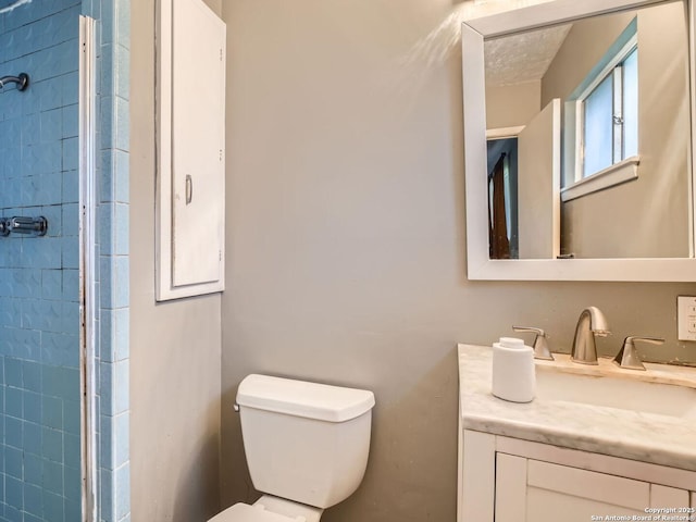 full bathroom with tiled shower, vanity, and toilet