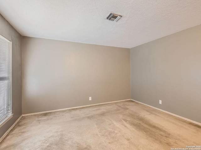 empty room featuring light colored carpet, visible vents, a textured ceiling, and baseboards