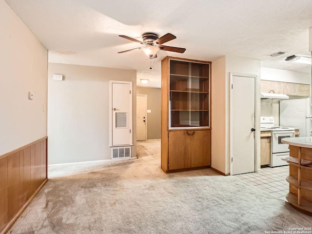 unfurnished living room featuring light carpet, ceiling fan, wainscoting, and visible vents