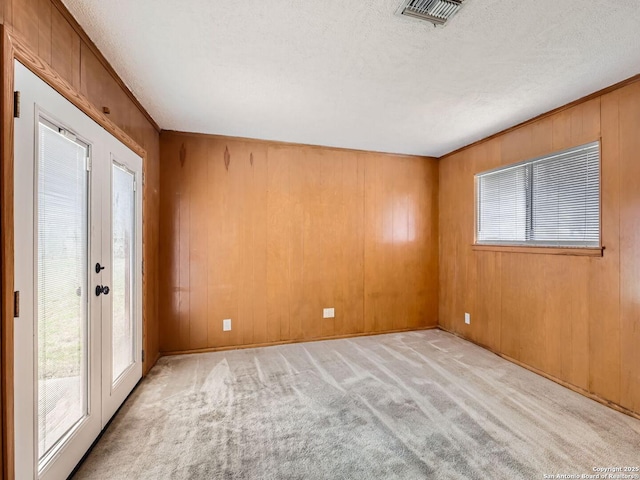 spare room with a textured ceiling, wooden walls, light colored carpet, visible vents, and french doors