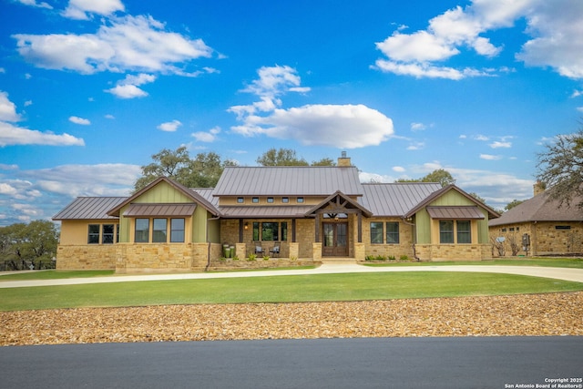 view of front of house featuring a chimney, a front yard, a standing seam roof, metal roof, and stone siding