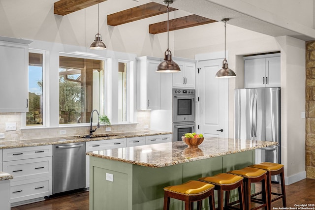 kitchen featuring decorative light fixtures, stainless steel appliances, a kitchen island, a sink, and light stone countertops