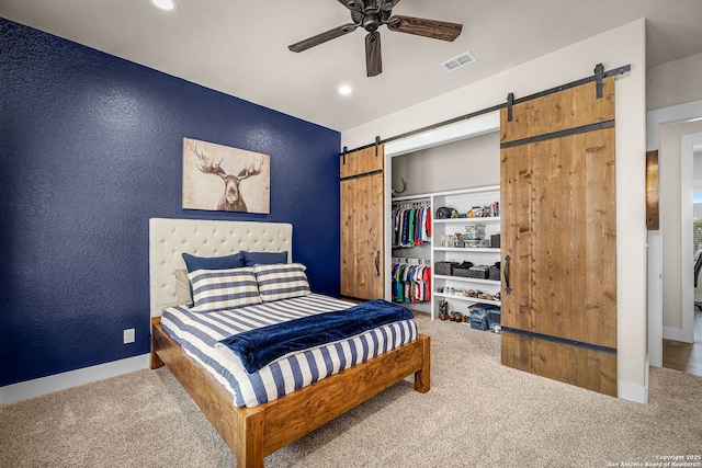 carpeted bedroom featuring a textured wall, a barn door, a closet, and visible vents