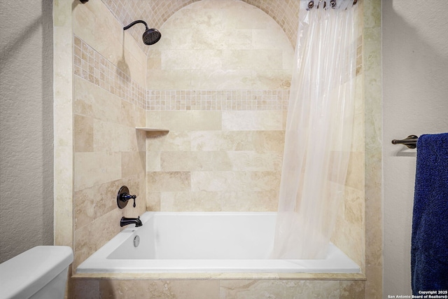 bathroom featuring a textured wall, tiled shower / bath combo, and toilet