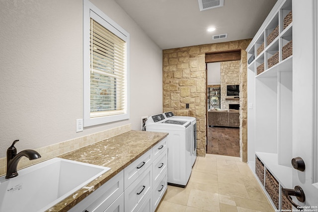 clothes washing area featuring cabinet space, visible vents, a sink, and washing machine and clothes dryer