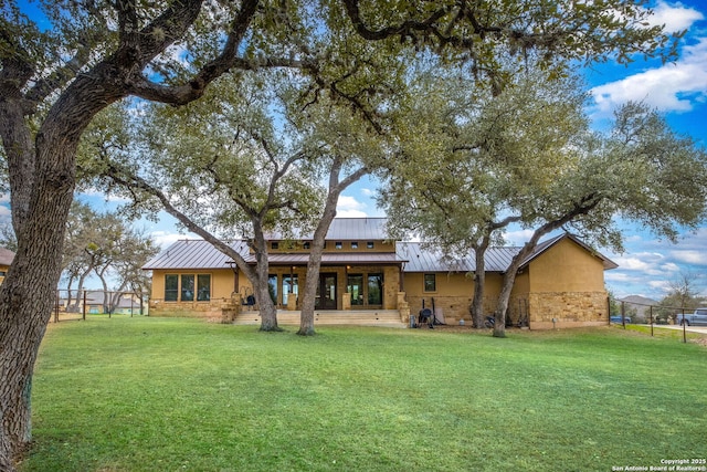 rear view of property with stone siding, a standing seam roof, and a lawn