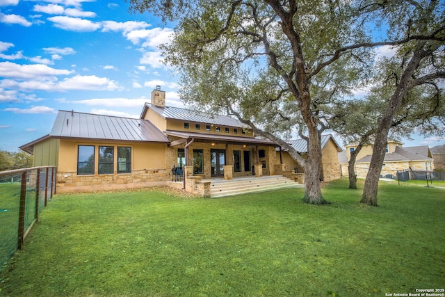 rear view of property featuring a yard, a standing seam roof, fence, metal roof, and stone siding