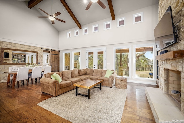 living area featuring a ceiling fan, wood finished floors, a stone fireplace, high vaulted ceiling, and beam ceiling