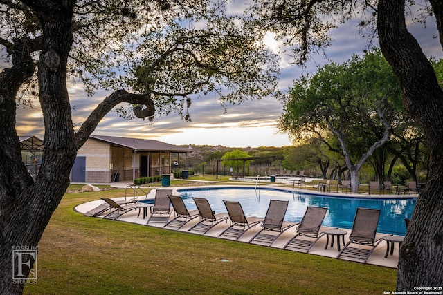 pool at dusk featuring a patio area, a community pool, and a lawn