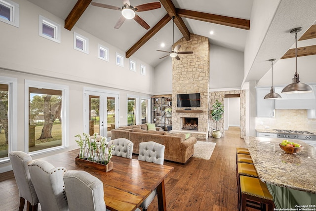 dining area featuring wood finished floors, a stone fireplace, french doors, high vaulted ceiling, and beam ceiling