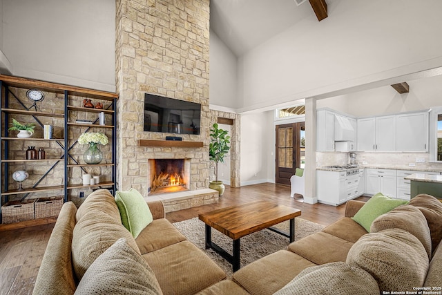 living area with baseboards, high vaulted ceiling, wood finished floors, and a stone fireplace