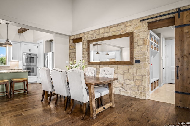 dining room featuring wood finished floors, a towering ceiling, and a barn door