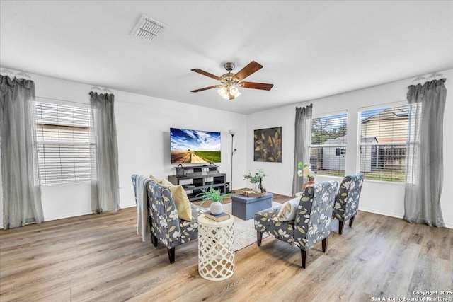 sitting room with light wood-style floors, baseboards, visible vents, and a ceiling fan