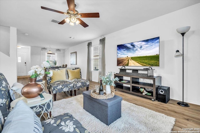 living room with light wood-style flooring, visible vents, and a ceiling fan