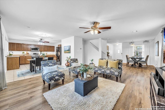 living room with light wood-type flooring, ceiling fan, and visible vents