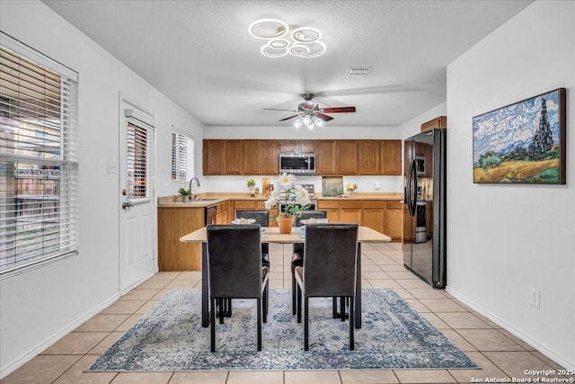 kitchen featuring light tile patterned flooring, black fridge with ice dispenser, visible vents, light countertops, and stainless steel microwave