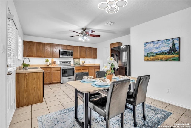 kitchen with light tile patterned floors, stainless steel appliances, light countertops, brown cabinetry, and a sink