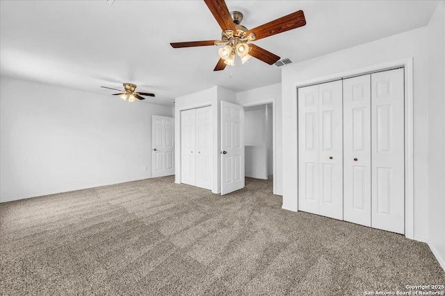 unfurnished bedroom with multiple closets, visible vents, carpet floors, and a ceiling fan