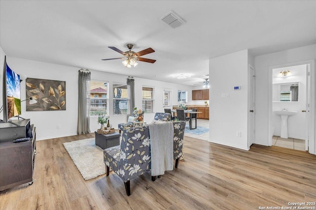 living area with light wood finished floors, baseboards, visible vents, and a ceiling fan