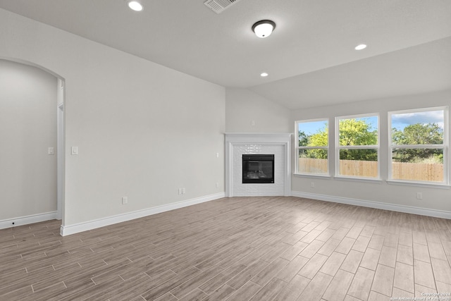 unfurnished living room with arched walkways, baseboards, a fireplace, and light wood finished floors