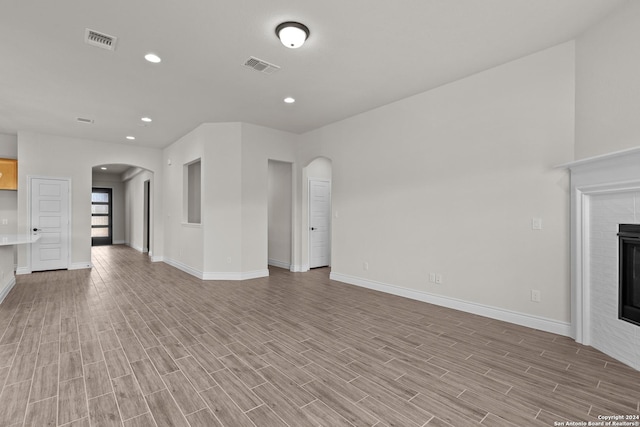 unfurnished living room with light wood-type flooring, arched walkways, visible vents, and a glass covered fireplace