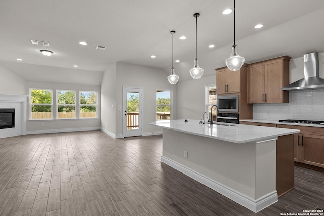 kitchen with light countertops, visible vents, a kitchen island with sink, a sink, and wall chimney range hood