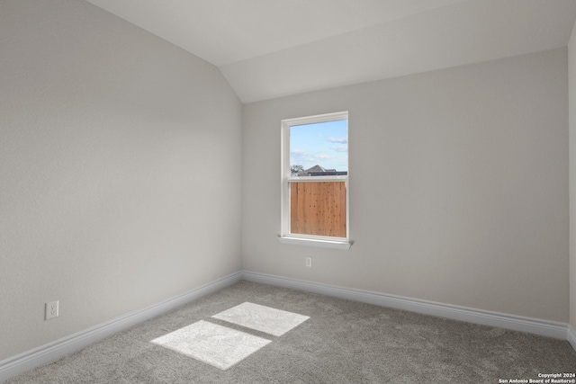 empty room featuring lofted ceiling, carpet flooring, and baseboards