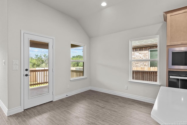 unfurnished dining area with light wood finished floors, baseboards, and vaulted ceiling