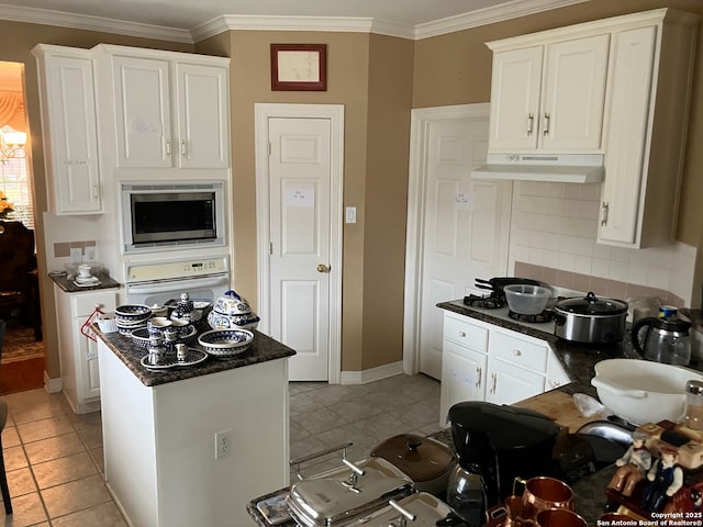 kitchen with dark countertops, stainless steel microwave, oven, under cabinet range hood, and white cabinetry