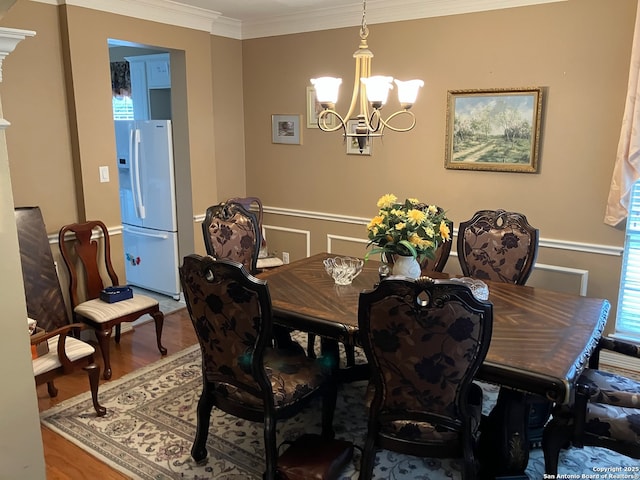 dining room with a decorative wall, wood finished floors, ornamental molding, wainscoting, and an inviting chandelier