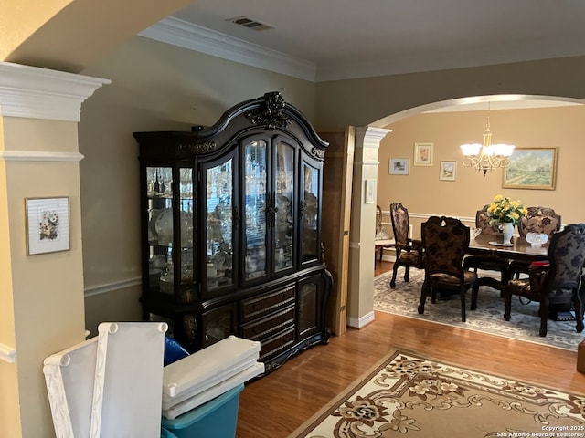 interior space featuring arched walkways, visible vents, ornamental molding, wood finished floors, and a chandelier