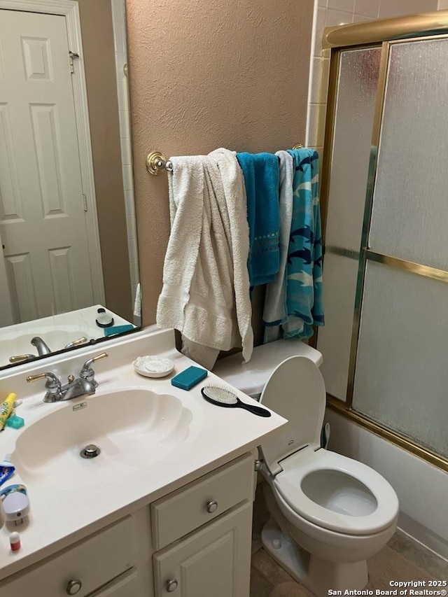 bathroom featuring toilet, vanity, enclosed tub / shower combo, and a textured wall