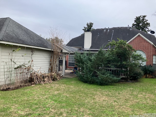 rear view of house featuring brick siding, a lawn, and a chimney