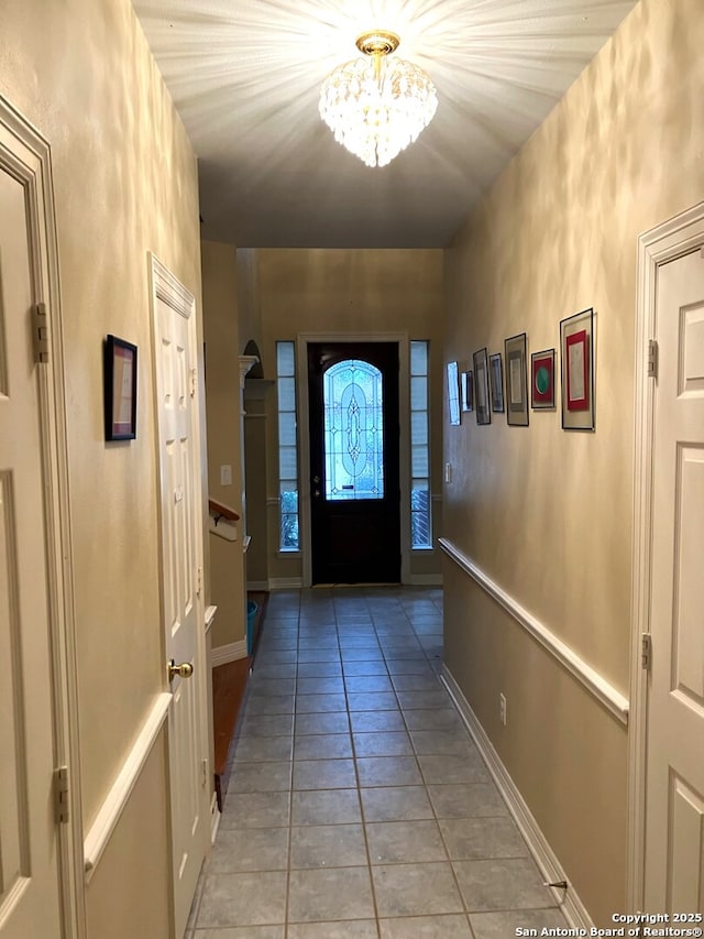 doorway to outside with baseboards, a notable chandelier, and light tile patterned flooring