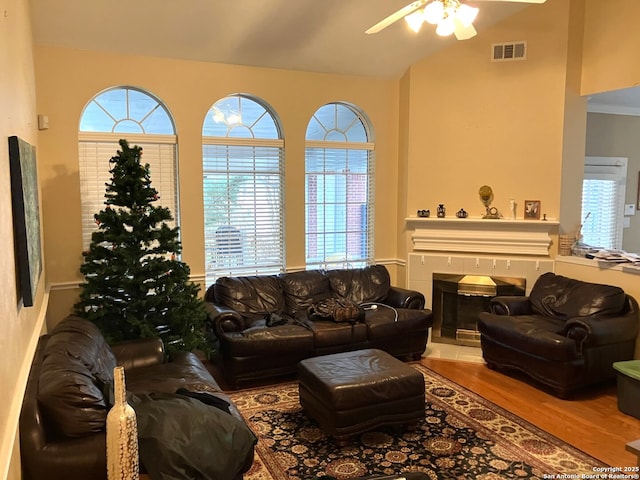 living room with light wood finished floors, visible vents, ceiling fan, vaulted ceiling, and a fireplace