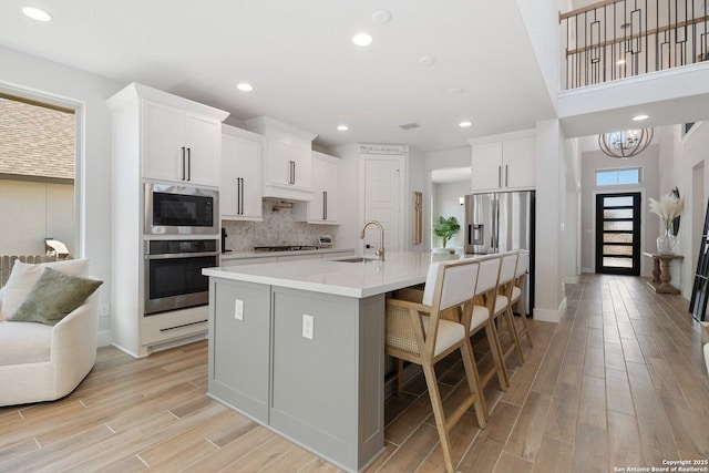 kitchen featuring light countertops, decorative backsplash, light wood-style flooring, stainless steel appliances, and a sink