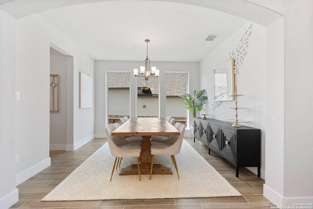 dining room with baseboards, visible vents, wood finish floors, arched walkways, and a notable chandelier