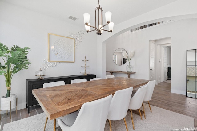 dining space with wood finished floors, visible vents, baseboards, arched walkways, and a notable chandelier