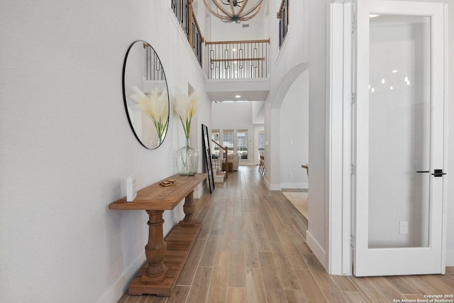 corridor with baseboards, arched walkways, wood finished floors, and stairs