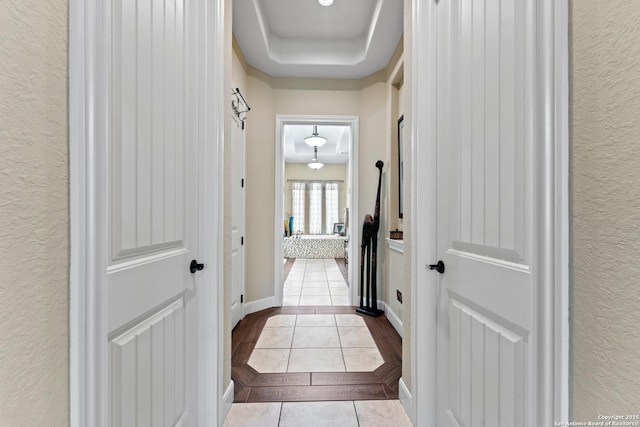 hallway featuring light tile patterned floors, baseboards, a raised ceiling, and a textured wall