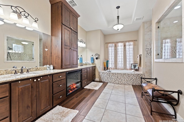 bathroom featuring a tray ceiling, visible vents, a bath, and vanity