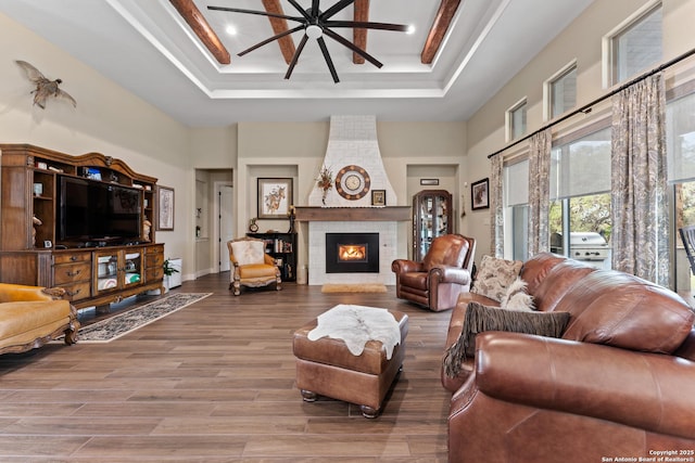 living area featuring a fireplace, a high ceiling, a raised ceiling, and wood finished floors