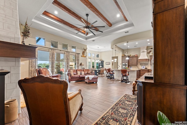 living area featuring ceiling fan, a tray ceiling, a fireplace, and light wood-style floors