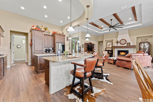 kitchen with a large fireplace, stainless steel fridge, a breakfast bar, decorative light fixtures, and light stone countertops