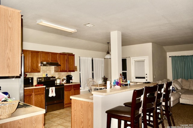 kitchen featuring open floor plan, black range with electric stovetop, a kitchen breakfast bar, a peninsula, and light countertops