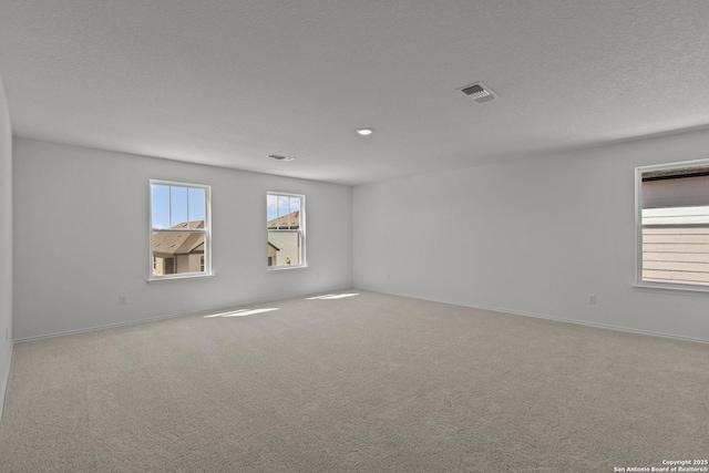 spare room with baseboards, visible vents, a textured ceiling, and light colored carpet